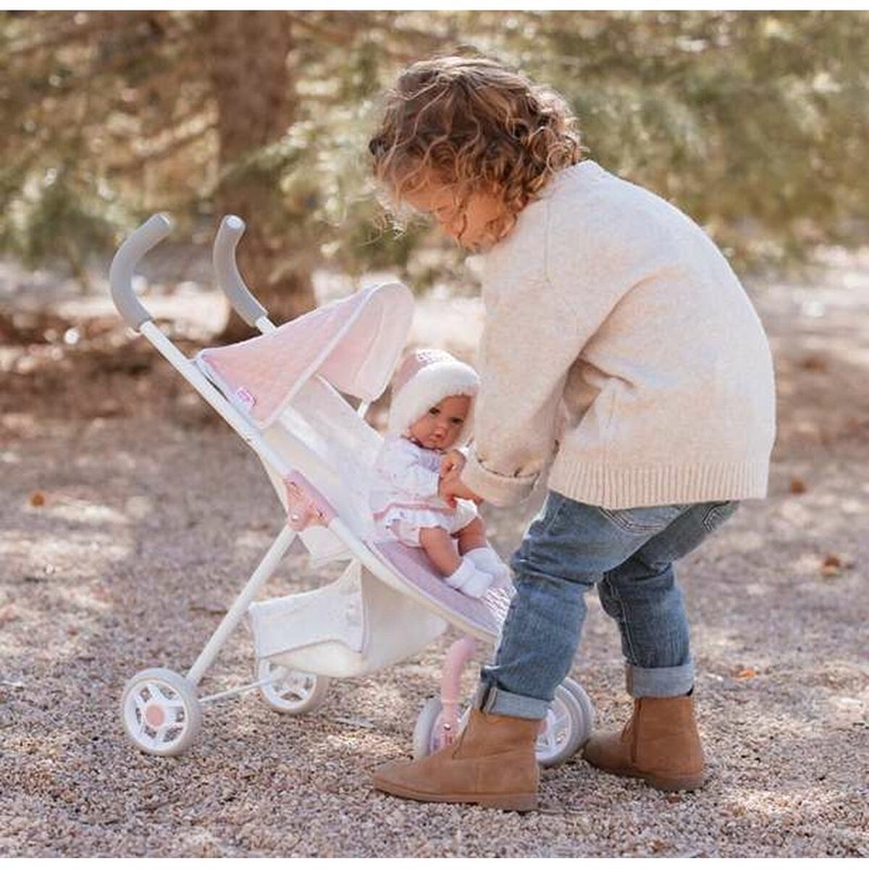 Niña feliz con su cochecito de juguete para muñecas en el parque